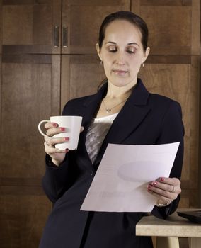 Business woman drinks coffee and reads a document.