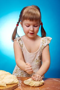 Smiling little girl kneading dough at kitchen with baking a pie