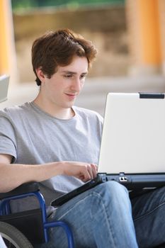 Disabled young man sitting in wheelchair using laptop