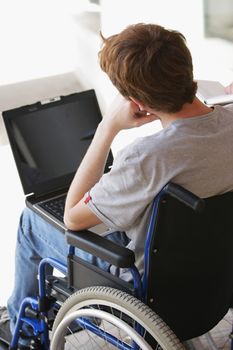 Disabled young man sitting in wheelchair using laptop