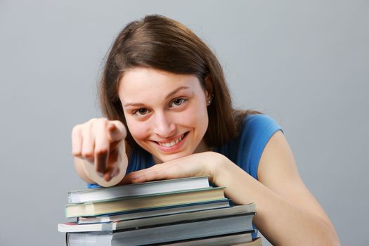 Beautiful girl student with stack of books pointing