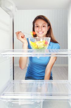 Beautiful healthy girl taking a salad from the refrigerator