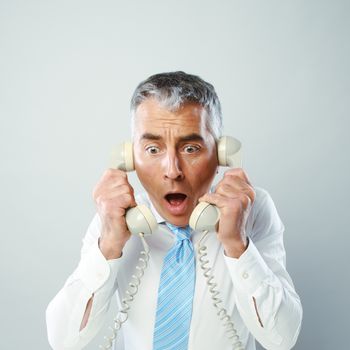 A stressed businessman talking in the two handsets that he is holding.