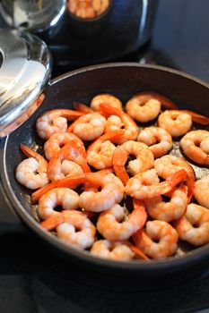 Photo of shrimp being fried in butter on a black frying pan. Shallow depth of field with focus across the middle.