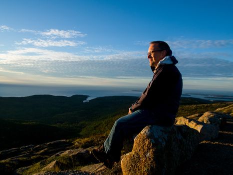 Man watching the sunrise over the sea on top of Cadillac Mountain in Acadia National Park