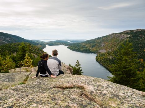 Couple sitting on top of a mountain over Jordan Pond lake in Acadia National Park
