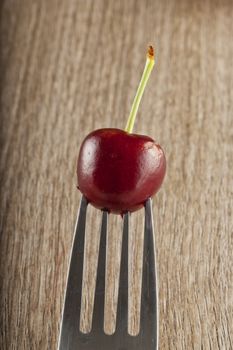 Single red cherry stuck on the prongs of a fork