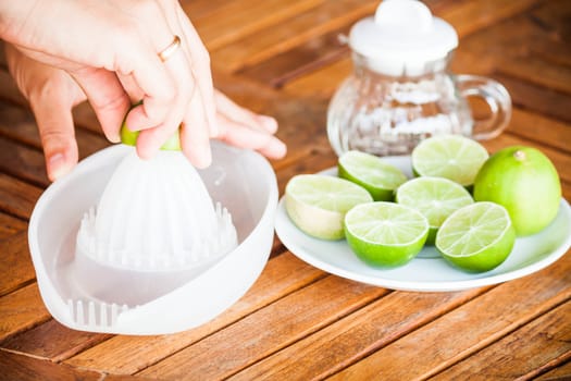 Hand squashing fresh citrus lime on wood table