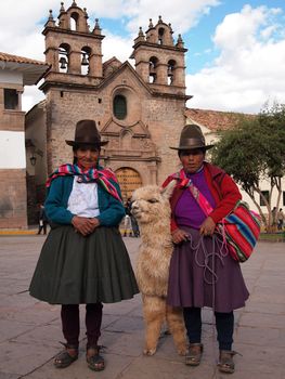 CUZCO, PERU – SEPTEMBER 18: Two indigenous women in traditional clothes  with hats and an alpaca in front of a church in Cuzco in Peru on September 18, 2011.