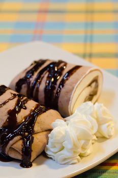 close up chocolate  crepe rolls  topping with chocolate  syrup served with whipping cream 