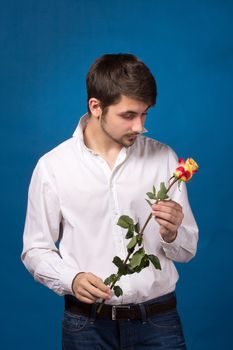 Young man looking to red rose on blue background