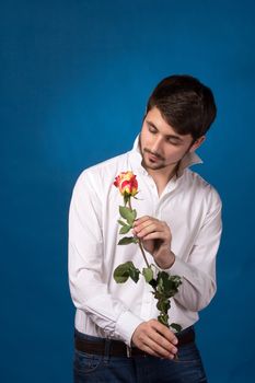 Young man looking to red rose on blue background