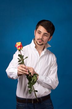 Young man looking to red rose on blue background