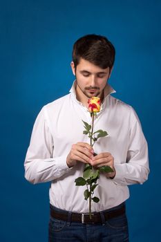 Young man looking to red rose on blue background