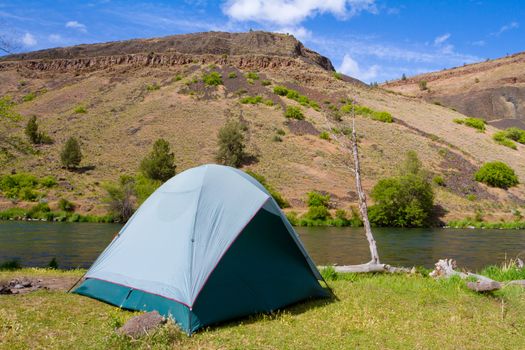 A rustic tent campsite on the Deschutes River in Oregon shows a tent setup next to a boat and the river. This is form a float camping trip.