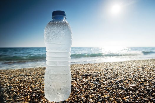 Bottle of fresh water is on the sand by the sea.