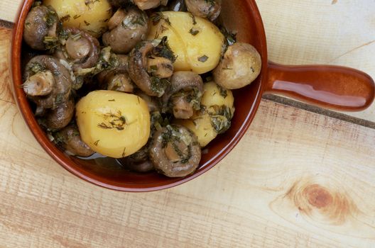 Delicious Stew with Champignon Mushrooms, Roasted Potato, Greens and Onion in Brown Frying Pan on Wood background. Top View
