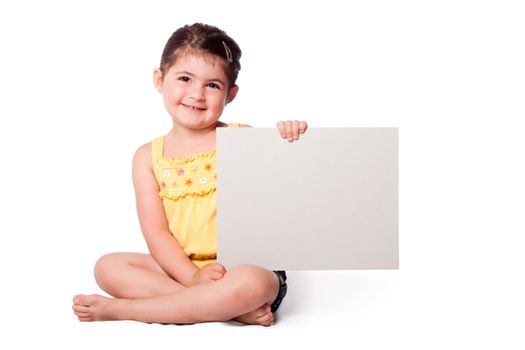 Cute happy smiling girl wearing summery yellow shirt sitting while holding whiteboard.
