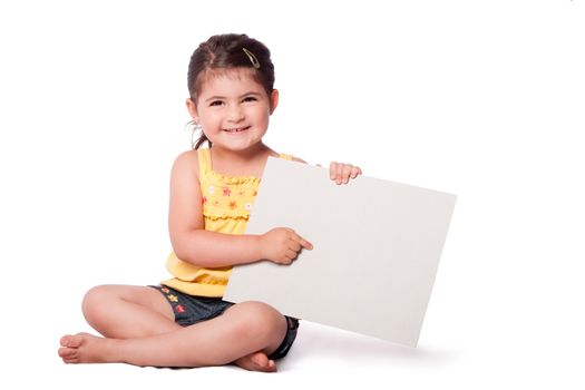 Cute happy smiling girl wearing summery yellow shirt sitting while holding and pointing at whiteboard.