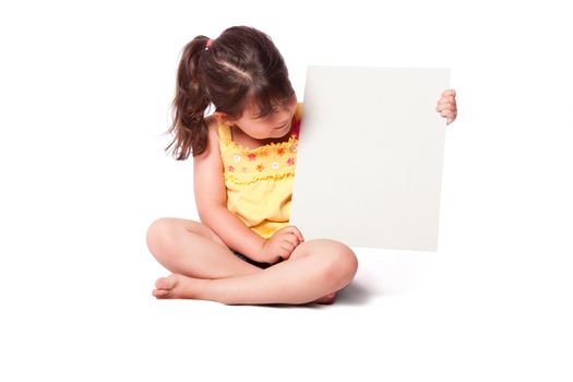 Cute girl wearing summery yellow shirt sitting while holding whiteboard and looking at it.