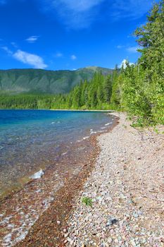 Small waves trickle through bright glacial rocks of Lake McDonald in Glacier National Park.