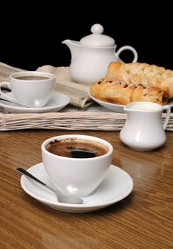 cup of fragrant black coffee on the table with newspaper and pastries
