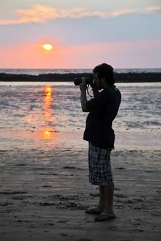 Vertical color portrait of young man taking pictures at sunset on the beach at Manori, Bombay, India