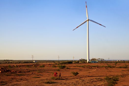 Horizontal color landscape captured in Gujarat India in the early morning before the sun rises of a group of women walking away across barren fields and a windmill generator