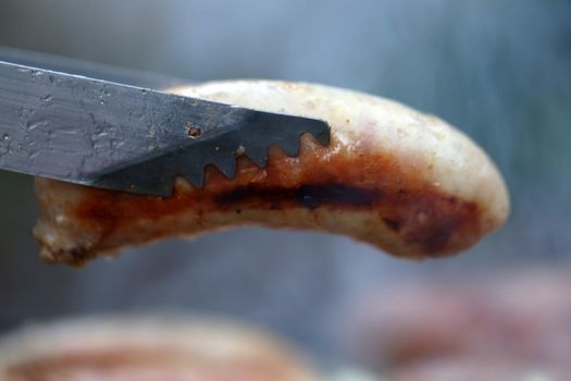 A barbecue tongs with sausege close-up