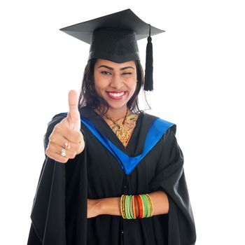 Happy Indian graduate student in graduation gown and cap giving thumb up hand sign. Portrait of beautiful Asian female model standing isolated on white background.