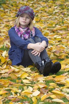 little girl sitting on leaves in the park