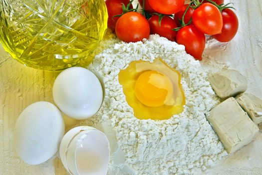 Ingredients for preparation of homemade egg pasta: flour, eggs, tomatoes and olive oil bottle.