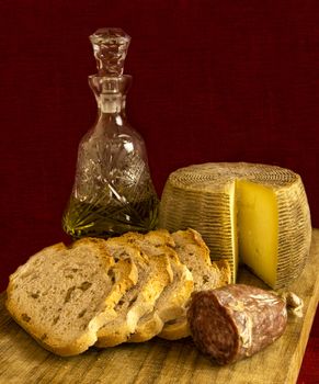 Mediterranean food: sheep cheese, salami, bread with walnuts and olive oil on a wooden cutting board on a dark red background.