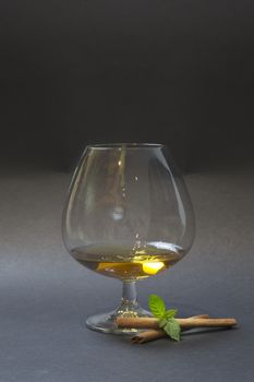 Balloon of cognac decorated with cinnamon stick and mint twig isolated on dark background.