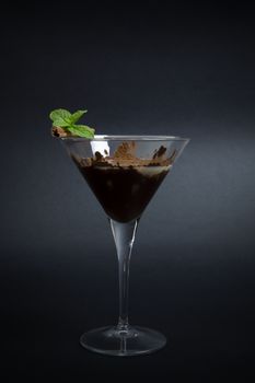 Cocktail made with chocolate liquor, banana liquor and coffee, decorated with cinnamon stick and mint twig, isolated on dark background.