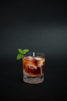 Cocktail made with vodka, red liquor and few drop of yogurt liquor on top, decorated with mint twig, isolated on dark background.