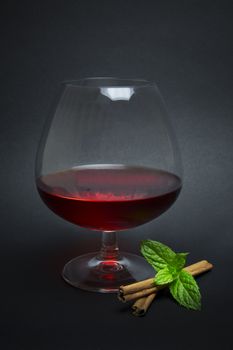 Cocktail made with red bitter liqueur, red vermouth and whiskey aged eight, decorated with cinnamon sticks and mint sprig, isolated on dark background.