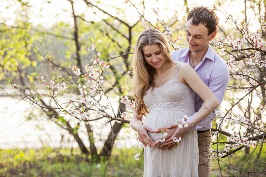 Young pregnant couple outdoors in spring blossom