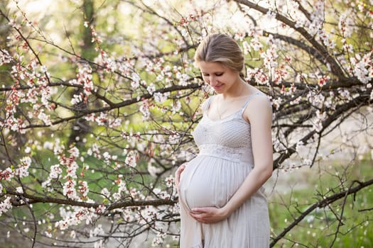 Young pregnant woman against blossoming tree in spring