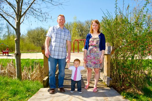 A man and a woman hold their baby one year old son while posing for a family photo outdoors.