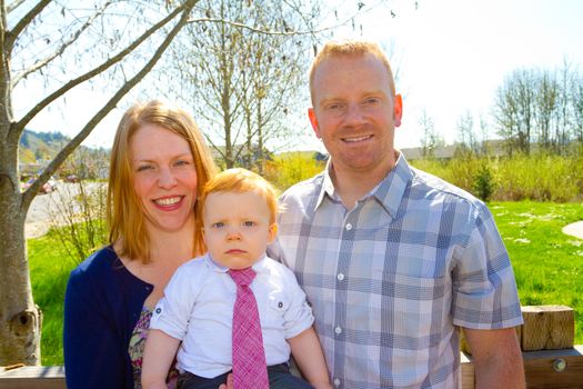 A man and a woman hold their baby one year old son while posing for a family photo outdoors.