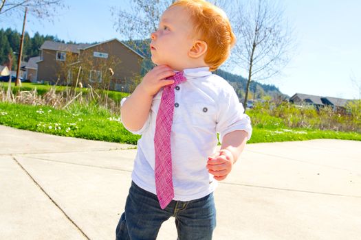 A baby boy plays at the park wearing his Sunday's best clothes including a tie around his neck.
