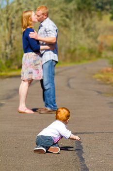 In this selective focus image the parents of a baby one year old boy are kissing out of focus in the background.