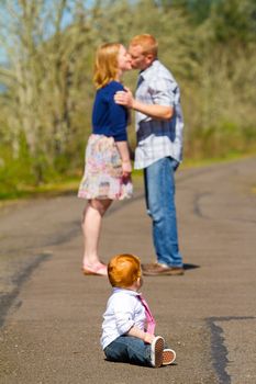 In this selective focus image the parents of a baby one year old boy are kissing out of focus in the background.
