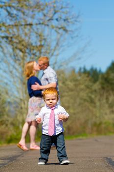 Parents are out of focus in this selective focus image while a baby boy runs toward the camera.