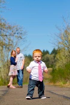 Parents are out of focus in this selective focus image while a baby boy runs toward the camera.