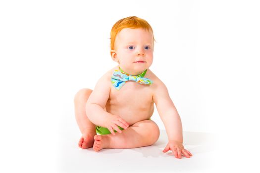 A one year old baby boy in the studio with a white background. The kid is wearing a bowtie and a diaper.