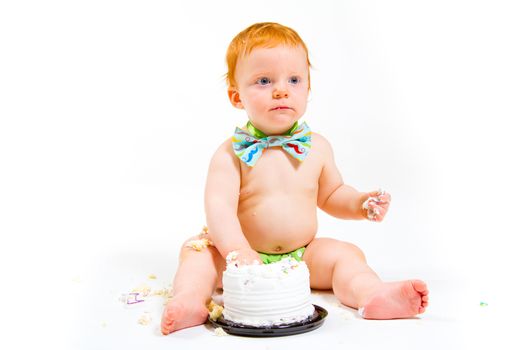 A baby boy gets to eat cake for the first time on his first birthday in this cake smash in studio against a white background.