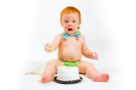 A baby boy gets to eat cake for the first time on his first birthday in this cake smash in studio against a white background.