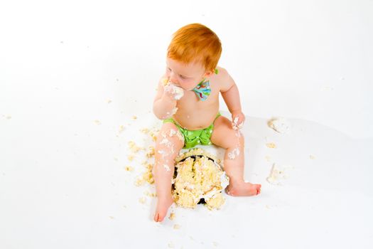 A baby boy gets to eat cake for the first time on his first birthday in this cake smash in studio against a white background.